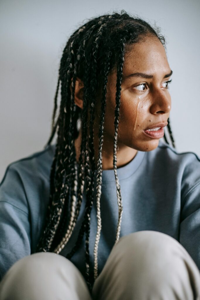 A pensive woman seated indoors, expressing emotion and concern.
